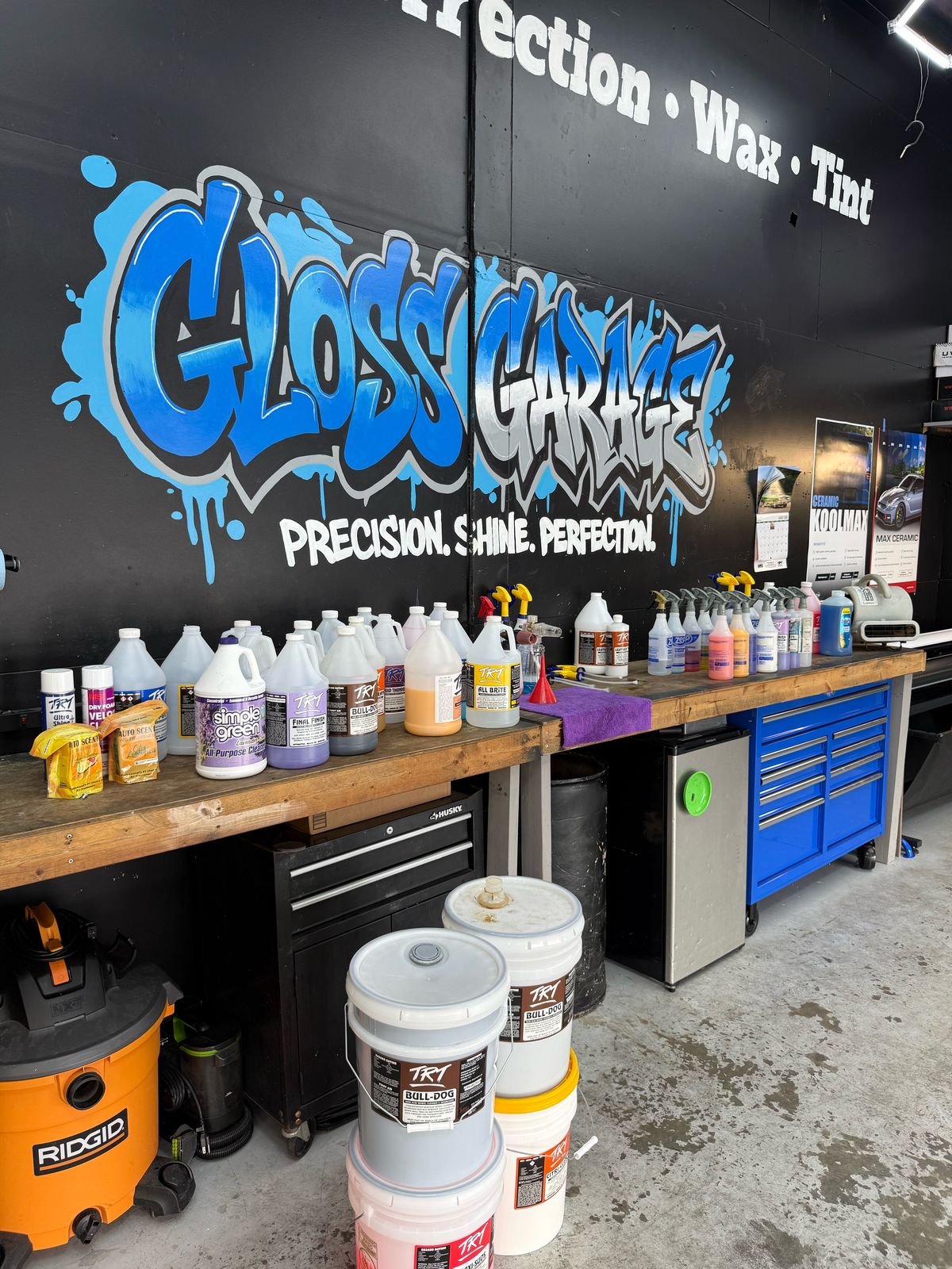 Workbench in the Gloss Garage shop stocked with professional detailing chemicals, wash buckets and a blue tool chest under the graffiti mural