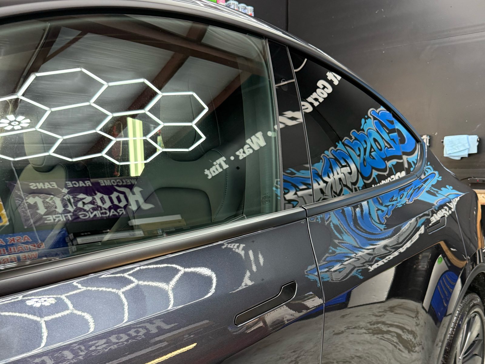 Ceramic-coated Tesla Model Y door reflecting the Gloss Garage mural and hex lights