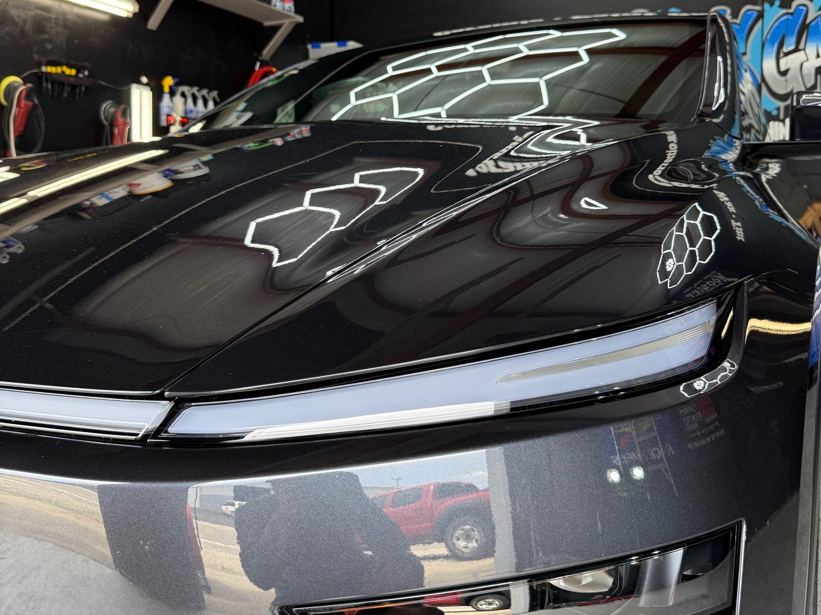 Close-up of a ceramic-coated Tesla Model Y hood with a mirror-like reflection of the hex lights