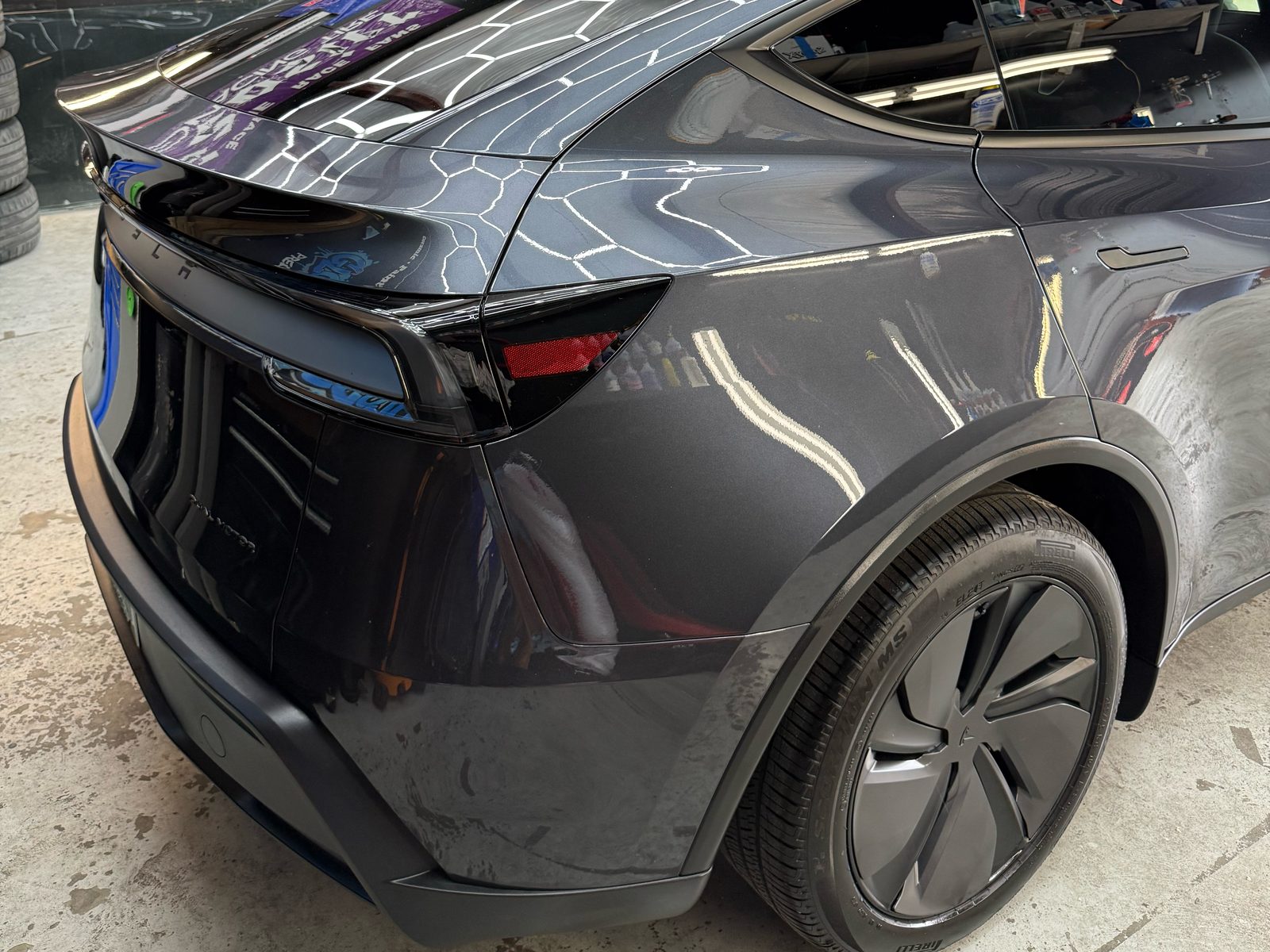 Rear quarter of a gray Tesla Model Y after ceramic coating, glossy paint reflecting the shop lights